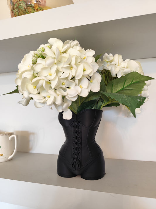 Black corset-shaped vase with white flowers on a shelf